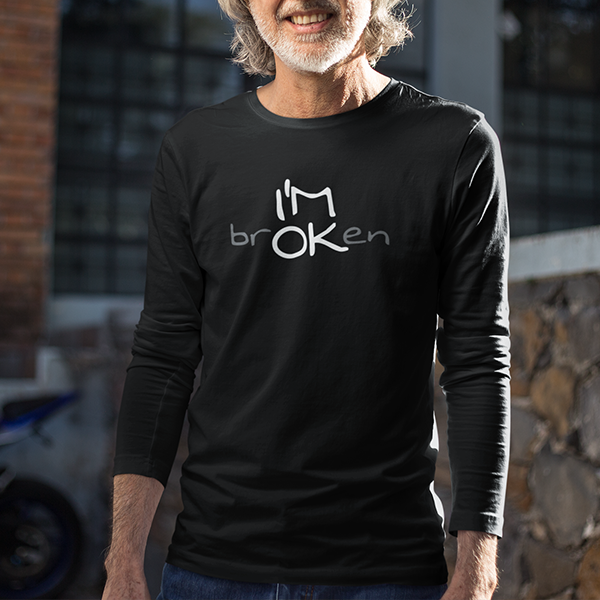 I'M brOKen Premium Sober Apparel worn by a smiling man in a black long-sleeve shirt, featuring a hidden "I'M OK" message that represents strength, recovery, and finding hope through life's challenges.