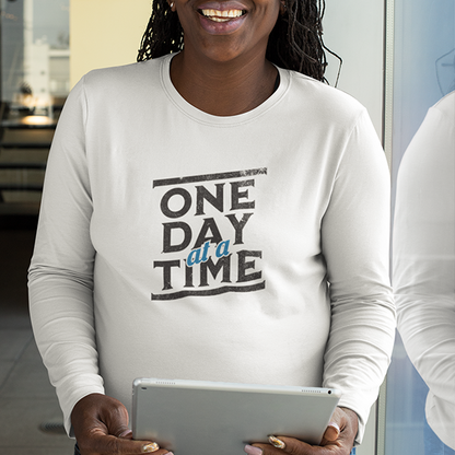 One Day At A Time Premium Sober Apparel worn by a woman in a white long-sleeve shirt, carrying an encouraging message of hope, perseverance, and daily progress.
