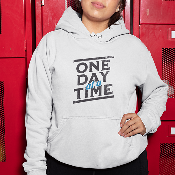 One Day At A Time Premium Sober Apparel worn by a man in a black hoodie, featuring a powerful recovery message that inspires hope, commitment, and progress one day at a time.