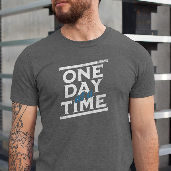 One Day At A Time Premium Sober Apparel worn by a man in a sports gray t-shirt, featuring a timeless recovery message that reminds us lasting change happens one day at a time.