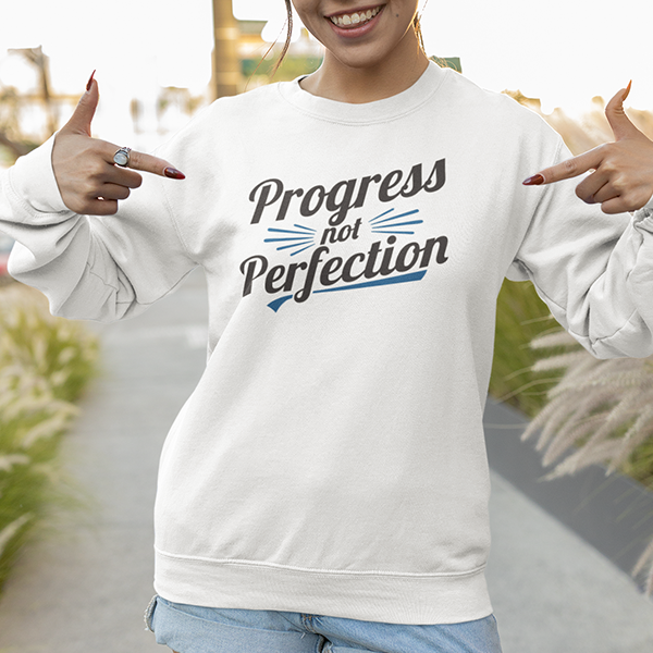 Model wearing a white sweatshirt featuring the text 'Progress Not Perfection' from Progress Not Perfection Premium Sober Apparel.
