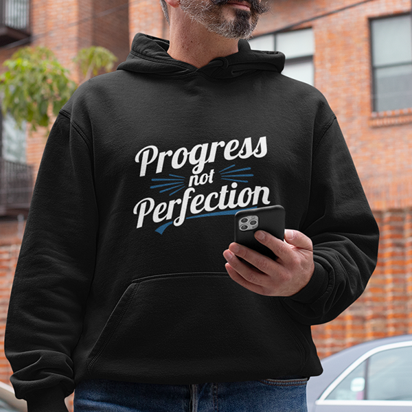 Person wearing Progress Not Perfection Premium Sober Apparel hoodie while holding a phone.